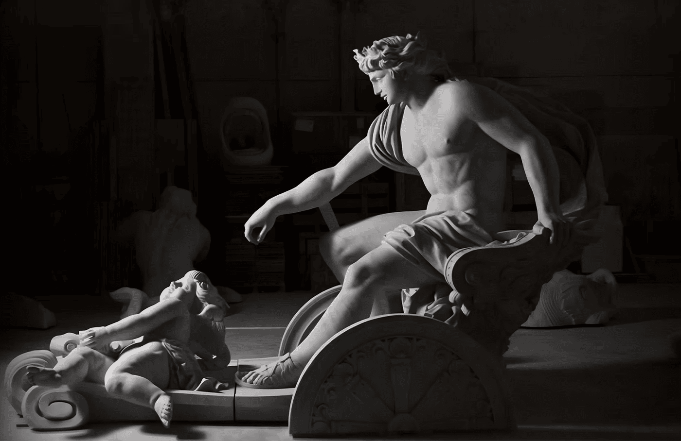A marble statue shows a muscular man seated in a chariot, reaching toward a small child who is lying in front of him, both figures dramatic and expressive amid a shadowy background.